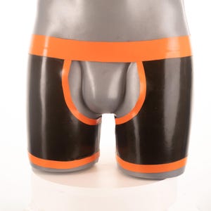May include: Black and orange latex boxer briefs. The underwear features a black body with orange trim around the waist, leg openings, and a front cutout. The garment is displayed on a mannequin.