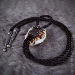 Back view of the Cat skull bolo tie on a grey faux fur fabric, oddities and curiosities gift, resin bone jewelry for dark academia and witchy style outfits.