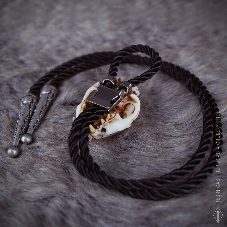 Back view of the Cat skull bolo tie on a grey faux fur fabric, oddities and curiosities gift, resin bone jewelry for dark academia and witchy style outfits.