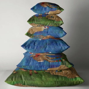 May include: A stack of six decorative throw pillows. Each pillow features a whimsical illustration of a reindeer with a blue background and a green grassy area. The reindeer has a red scarf and a brown body.