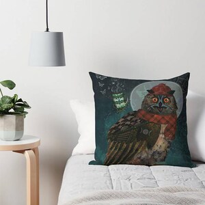 May include: Decorative throw pillow featuring a whimsical owl illustration. The owl is adorned with a red plaid scarf and hat, set against a dark teal background with a full moon and a floating teacup. The pillow is square.