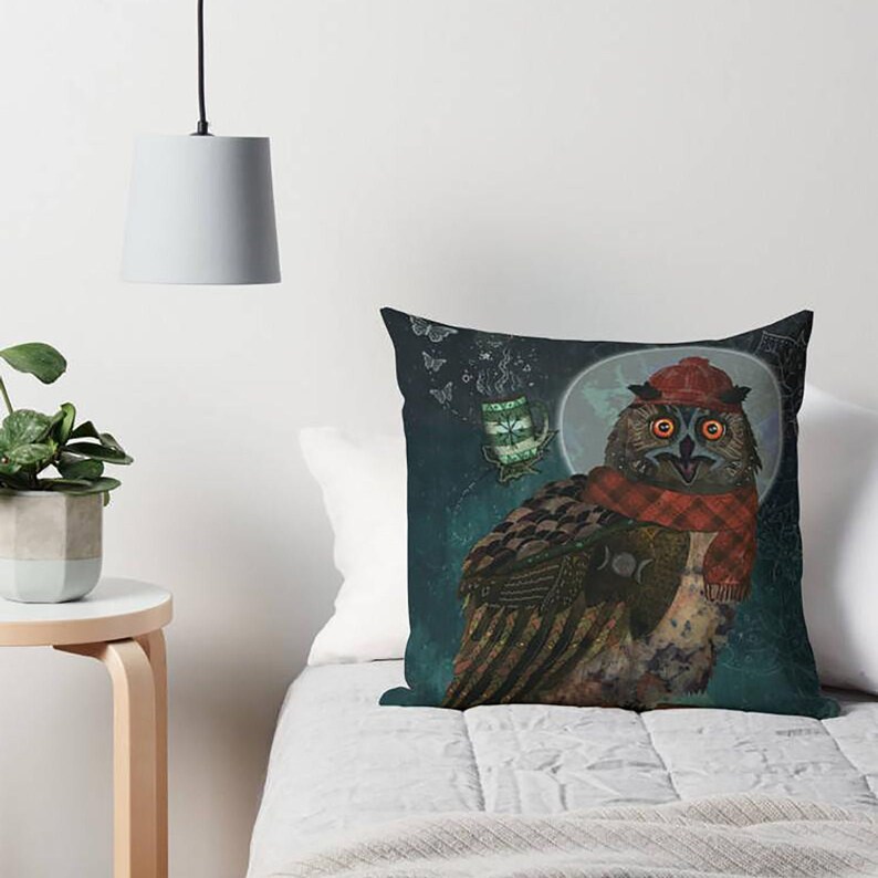 May include: Decorative throw pillow featuring a whimsical owl illustration. The owl is adorned with a red plaid scarf and hat, set against a dark teal background with a full moon and a floating teacup. The pillow is square.