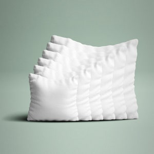 May include: A stack of seven square, white pillows. The pillows are arranged in a diagonal line, with each pillow slightly behind and to the right of the previous one. The pillows have a soft, textured appearance, suggesting a comfortable filling.