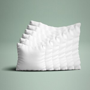 May include: A collection of seven white square pillows arranged in a diagonal row. The pillows are made of a soft, textured fabric and are evenly spaced. The background is a solid, muted green.
