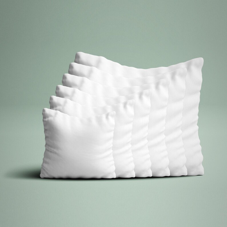 May include: A collection of seven white square pillows arranged in a diagonal row. The pillows are made of a soft, textured fabric and are evenly spaced. The background is a solid, muted green.