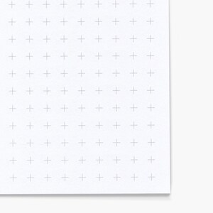 May include: A white sheet of paper with a grid of light gray plus signs. The paper has a slightly textured surface and a corner is folded over, revealing a clean white edge.