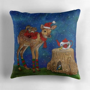 May include: Decorative throw pillow with a whimsical Christmas scene. A deer wearing a Santa hat and scarf has a squirrel on its back. A teapot sits on a tree stump with a bird. The background is a dark blue with white stars.