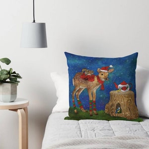 May include: Decorative throw pillow featuring a whimsical illustration of a deer wearing a Santa hat and scarf, with a squirrel on its back. A teapot and birds are also depicted. The pillow has a blue background with white dots.