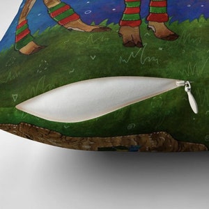 May include: Throw pillow featuring a whimsical illustration of deer legs wearing red and green striped leg warmers, standing on a grassy hill under a starry night sky. The pillow has a white zipper and a soft, textured appearance.