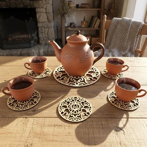 5 wooden coasters and one big coaster are placed on the table. Teacups are placed on 4 coasters and a kettle is placed on a big coaster. The laser cut coaster are cut with floral motifs.