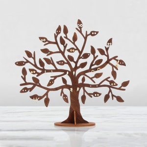 Dark brown laser cut wooden jewelry holder. The tree has holes for earrings. Other jewelry can be hung on the branches. Several pairs of earrings are hung on the tree.