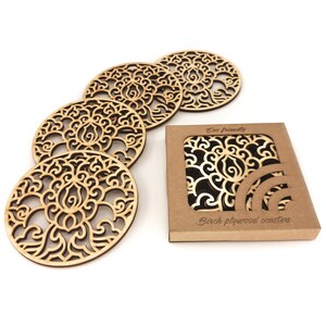 A set of wooden laser-cut coasters in a cardboard box. Placemats are cut out with floral motifs. The set includes 4 round coasters.