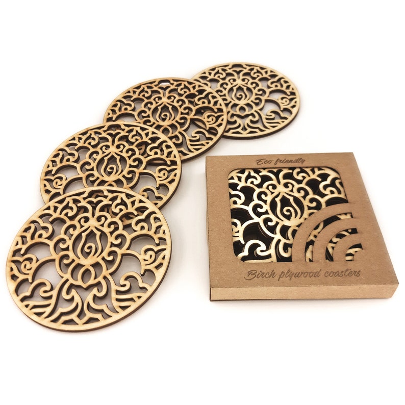 A set of wooden laser-cut coasters in a cardboard box. Placemats are cut out with floral motifs. The set includes 4 round coasters.
