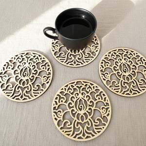 4 wooden coasters are placed on the table. A cup of tea placed on one coaster. Placemats are cut out with floral motifs.
