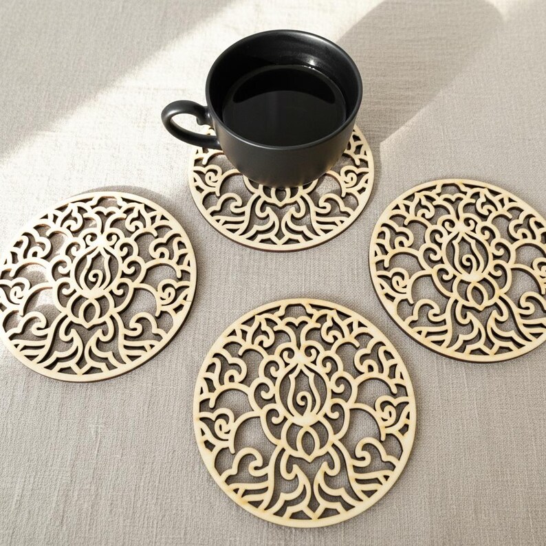 4 wooden coasters are placed on the table. A cup of tea placed on one coaster. Placemats are cut out with floral motifs.