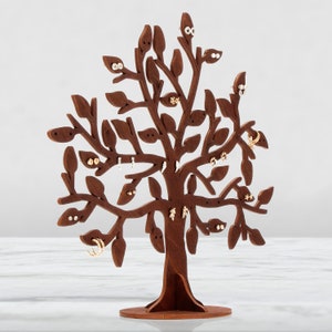 Dark brown laser cut wooden jewelry holder. The tree has holes for earrings. Other jewelry can be hung on the branches. Several pairs of earrings are hung on the tree.