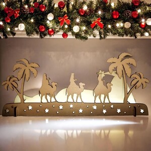 A Christmas garland can be seen in the background. The 3 Kings decoration stands nearby. Decoration of the three wise kings by candlelight.