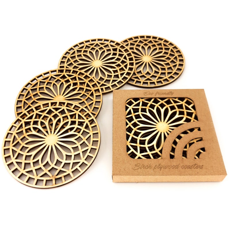 A set of wooden laser-cut coasters in a cardboard box. Placemats are cut out with modern flower motifs. The set includes 4 round drink coasters.