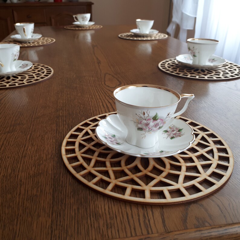 6 big wooden coasters are placed on the table. Coffee cups are placed on coasters. Laser-cut coasters are cut with modern floral motifs.