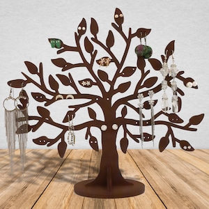 Dark brown laser cut wooden jewelry holder. The tree has holes for earrings. Other jewelry can be hung on the branches. Several pairs of earrings are hung on the tree.