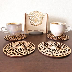 4 wooden coasters are placed on the table. Tea cups are placed on 2 coasters. There is a coaster holder with coasters inside. Placemats are cut out with modern flower motifs.