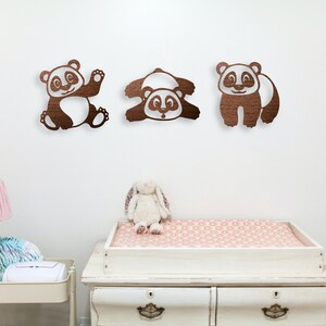 In the baby's room, pandas wall art hangs above the baby's changing table. Laser cut pandas wall art featuring three fun pandas are made of wood.