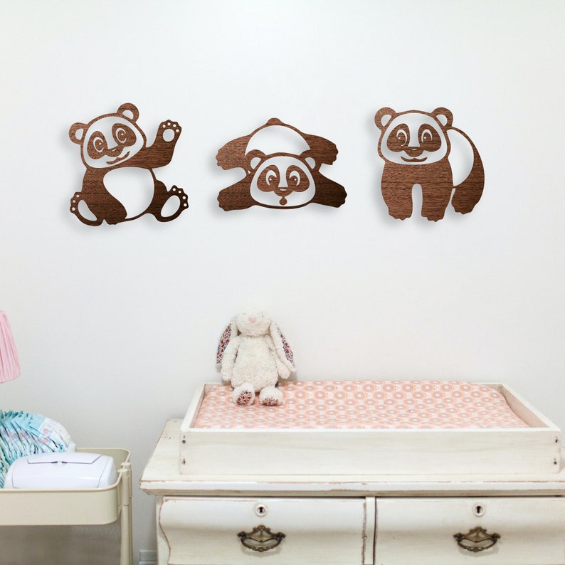 In the baby's room, pandas wall art hangs above the baby's changing table. Laser cut pandas wall art featuring three fun pandas are made of wood.