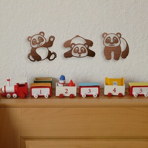 Pandas wall art hangs above the table with train in the kid's room. Laser cut pandas wall art featuring three fun pandas are made of wood.