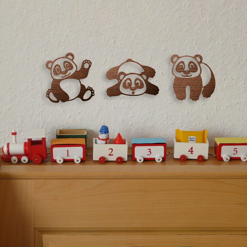Pandas wall art hangs above the table with train in the kid's room. Laser cut pandas wall art featuring three fun pandas are made of wood.