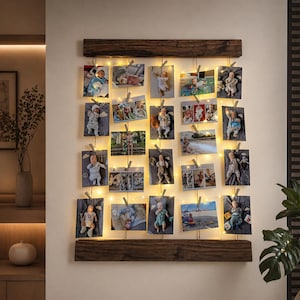 Könnte beinhalten: Ein rustikaler Holz-Fotorahmen mit mehreren Babyfotos, die an Schnüren befestigt sind und von kleinen Lichterketten beleuchtet werden. Der Rahmen hat oben und unten einen dunkelbraunen Holzrahmen. Die Fotos sind in verschiedenen Größen und Ausrichtungen.