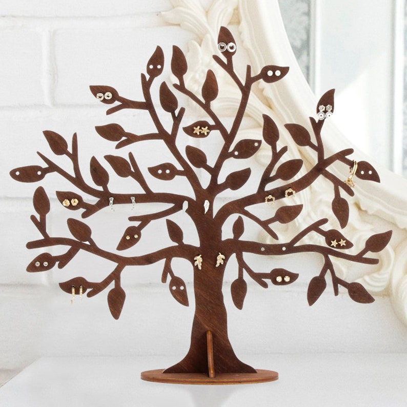 Dark brown laser cut wooden jewelry holder. The tree has holes for earrings. Other jewelry can be hung on the branches. Several pairs of earrings are hung on the tree.