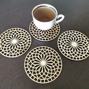 4 wooden coasters are placed on the table. A cup of tea placed on one coaster. Placemats are cut out with modern flower motifs.