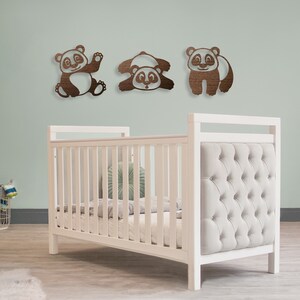 The baby's room has pandas wall art hanging above the baby's crib. Laser cut pandas wall art featuring three fun pandas are made of wood.