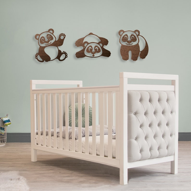The baby's room has pandas wall art hanging above the baby's crib. Laser cut pandas wall art featuring three fun pandas are made of wood.