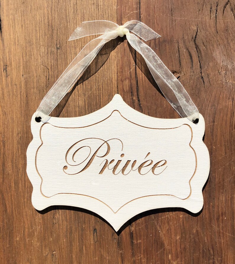 Puede incluir: Un letrero de madera blanco con un borde decorativo y la palabra "Priv&eacute;e" escrita en cursiva. El letrero est&aacute; colgado de una cinta blanca.
