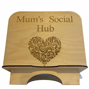 May include: A wooden stand with a cut-out heart design and the text "Mum's Social Hub" engraved on the front. The stand is made of light wood and has a natural finish.