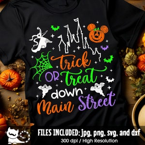 Puede incluir: Camiseta negra con temática de Halloween con la frase "Trick or Treat down Main Street" en naranja, verde y morado. El diseño incluye una calabaza, fantasmas, murciélagos y una telaraña. Es una prenda festiva.
