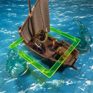 May include: A miniature wooden ship with a brown sail and a crew of miniature figures. The ship is floating on a blue and green water surface with two green translucent figures on either side. The ship has the text "Wizard Works" on the side. The ship is surrounded by a green plastic frame.