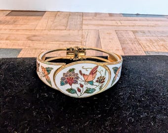 May include: A gold-toned hinged bracelet with a white enamel base. The bracelet features a floral and butterfly design in red, orange, green, and blue. The clasp is gold-toned.