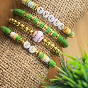 May include: A set of four bracelets with green and white beads, gold beads, and white letter beads spelling "TYLER" and "25". A white baseball charm is also included.