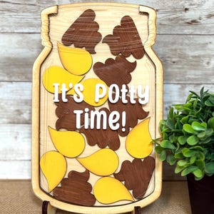 May include: Wooden jar-shaped sign with the text "It's Potty Time!" in white. The jar is filled with brown and yellow shapes. The sign is supported by a wooden stand.