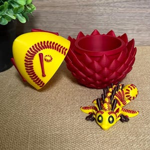 May include: A yellow and red softball-themed container set. The set includes a softball-shaped container, a red lotus-shaped container, and a yellow and red lizard figurine. The softball container has red stitching details.