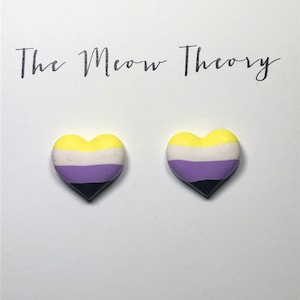 Könnte beinhalten: Ein Paar herzförmige Ohrringe mit den Farben der Non-Binary-Pride-Flagge. Die Ohrringe sind gelb, weiß, lila und schwarz.