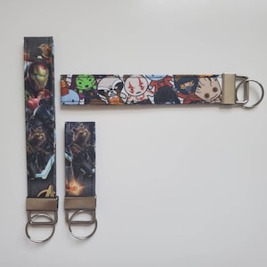 May include: Two keychains with different designs. One keychain features a colorful pattern of cartoon characters from the Marvel Cinematic Universe. The other keychain features a black and white pattern of characters from the Marvel Cinematic Universe. Both keychains have silver key rings.