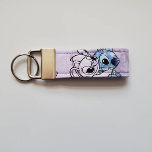 Op de afbeelding: Paarse en blauwe stoffen sleutelhanger met een cartoon afbeelding van Stitch en Angel uit de Disney-film Lilo & Stitch.