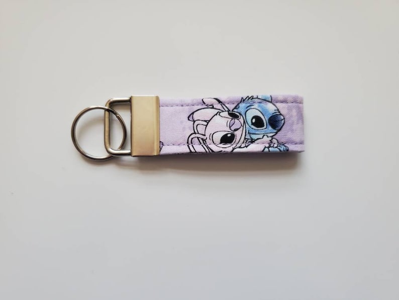 Op de afbeelding: Paarse en blauwe stoffen sleutelhanger met een cartoon afbeelding van Stitch en Angel uit de Disney-film Lilo & Stitch.