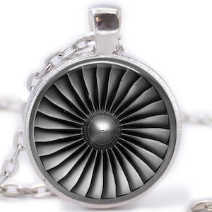 May include: Silver-toned pendant necklace featuring a detailed jet engine turbine design. The pendant is circular with a grayscale image of the turbine blades. The chain is also silver and hangs against a white background.