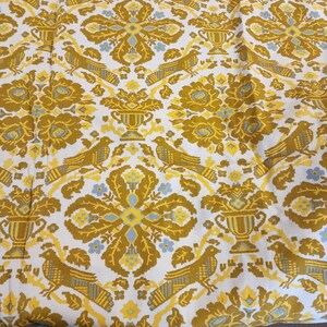 May include: White fabric with a repeating pattern of gold and blue stylized flowers, birds, and urns. The pattern is woven into the fabric.
