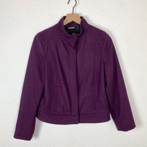 May include: A purple wool jacket with a zipper closure and a stand-up collar. The jacket has two pockets on the front and a black trim around the collar and pockets.
