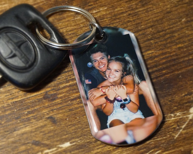 May include: A keychain with a clear plastic tag featuring a photo of a couple. The couple is smiling and hugging. The keychain is attached to a silver key ring.